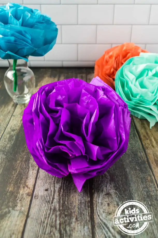 One Mexcian tissue paper flower displayed on a vase and other pom poms flowers are displayed in front of the vase
