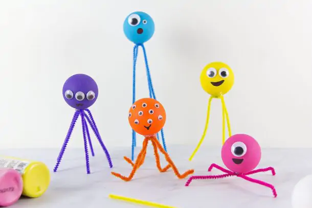 Ping pong ball monsters craft- yellow monster with a yellow pipe cleaner and google eyes, a yellow ping pong ball with white pipe cleaners, blue ping pong ball with blue pipe cleaners, and a red pipe cleaner with a red ping pong ball, ping pong ball pink with pink pipe cleaners