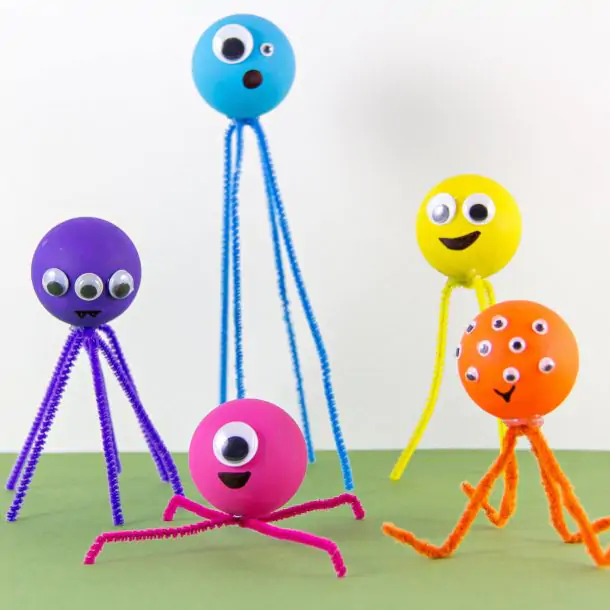 Ping pong ball monsters craft- yellow monster with a yellow pipe cleaner and google eyes, a yellow ping pong ball with white pipe cleaners, blue ping pong ball with blue pipe cleaners, and a red pipe cleaner with a red ping pong ball, ping pong ball pink with pink pipe cleaners