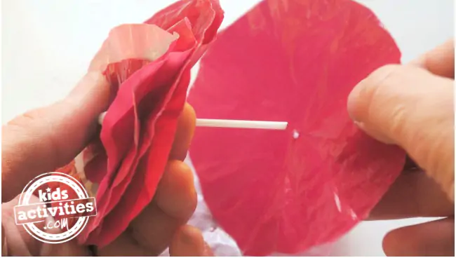 Step 2 - plastic flower craft for kids - Kids Activities Blog - Q tip threaded with various sizes layers of red plastic bag circles being added (in process)