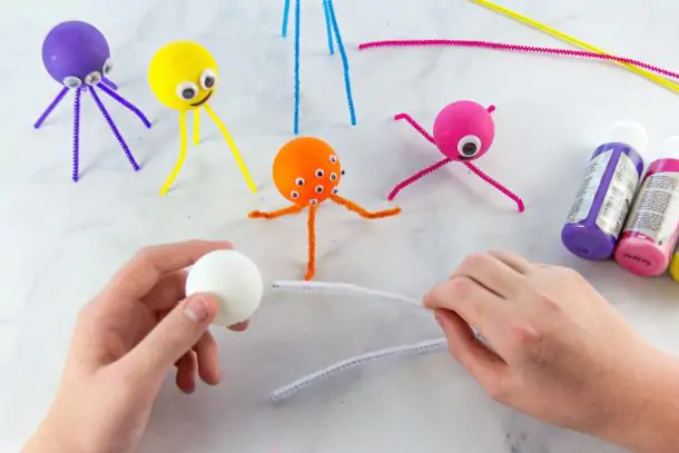 Ping pong ball monsters craft- yellow monster with a yellow pipe cleaner and google eyes, a yellow ping pong ball with white pipe cleaners, blue ping pong ball with blue pipe cleaners, and a red pipe cleaner with a red ping pong ball, ping pong ball pink with pink pipe cleaners